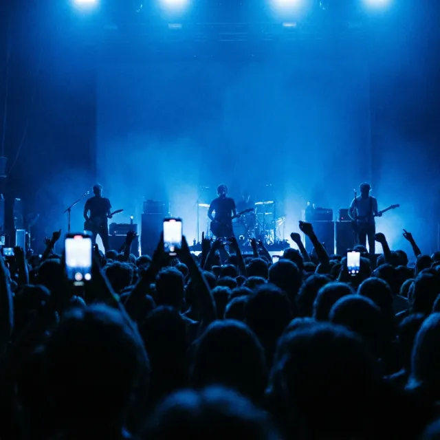 From the crowd — Raised hands and phone screens, the stage glowing past them.