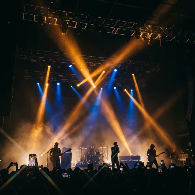 Stage beams — Hard beams cutting through haze, the band small beneath them.